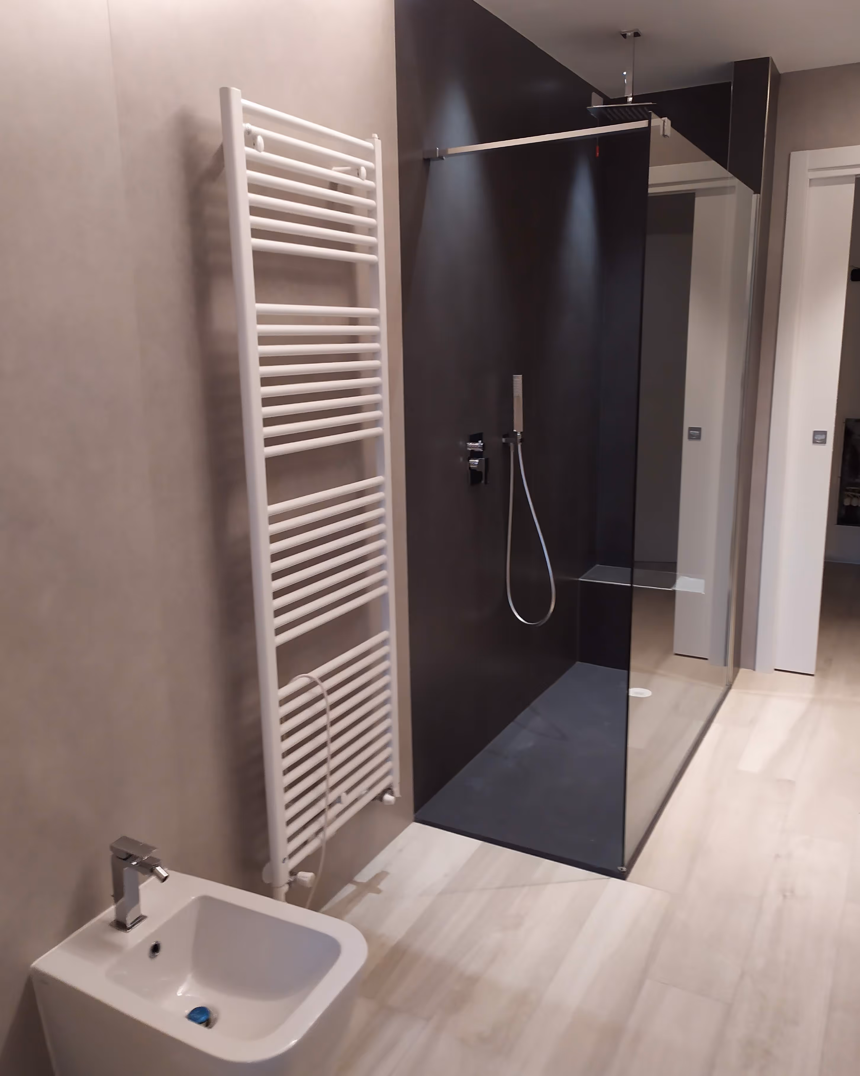 Bagno moderno con bidet bianco, termosifone a parete e doccia con parete di vetro scuro.