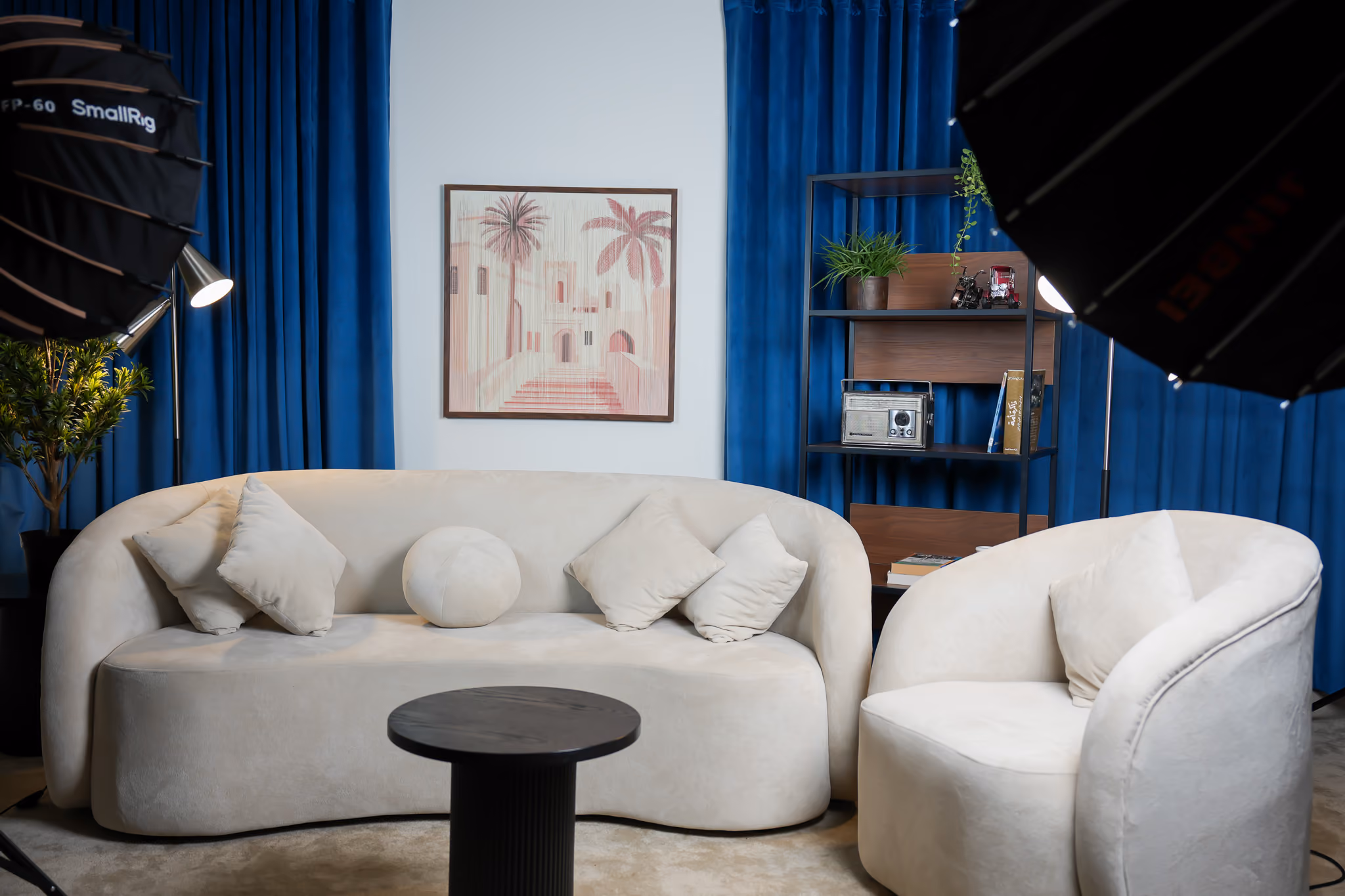 Sofa podcast setup with blue curtains, wall art and a shelf in the background