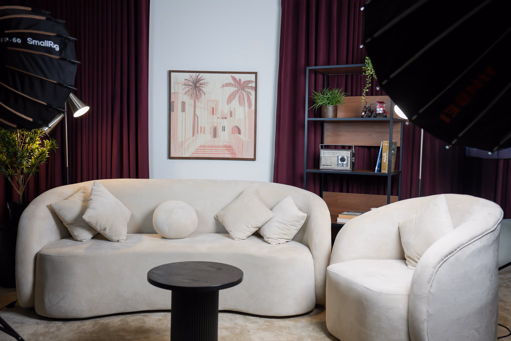 Sofa podcast setup with maroon curtains, wall art and a shelf with props in the background