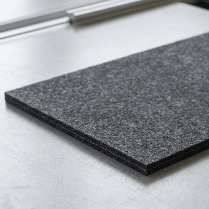 Carré de feutre gris foncé posé sur une surface métallique claire.