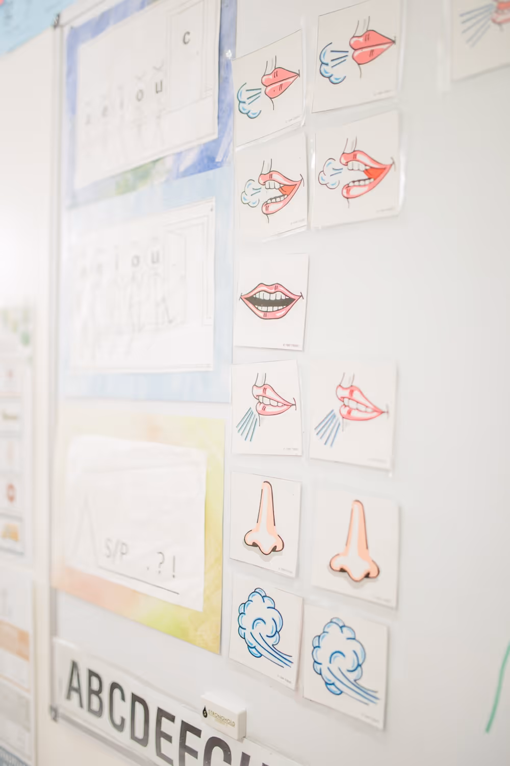 Wall with illustrated cards showing various mouth, nose, and breath actions for speech therapy or language learning.