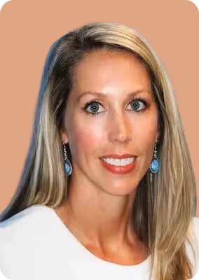 Woman with long blonde hair, blue eyes, wearing blue earrings and a white top against a peach background.
