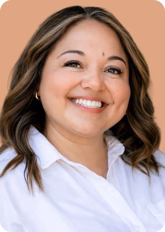 Smiling woman with wavy brown hair wearing white collared shirt and small hoop earrings.