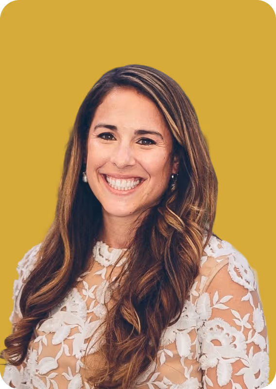Smiling woman with long wavy hair wearing a white floral lace top against a solid mustard background.