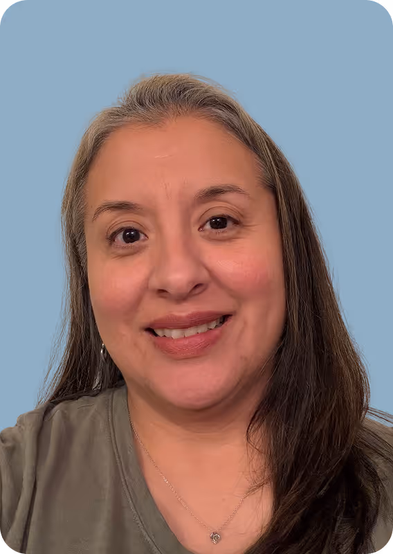 Smiling woman with long hair wearing a green shirt and a necklace against a light blue background.