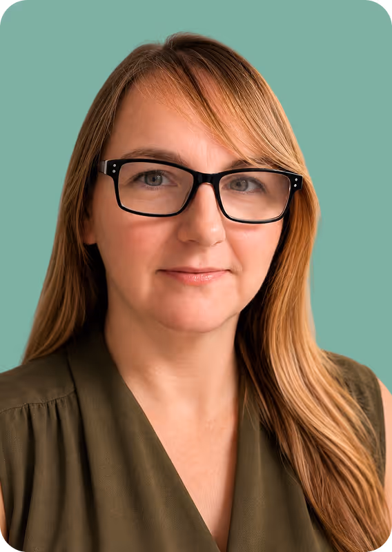 Woman with long light brown hair wearing black glasses and an olive green sleeveless top on a teal background.