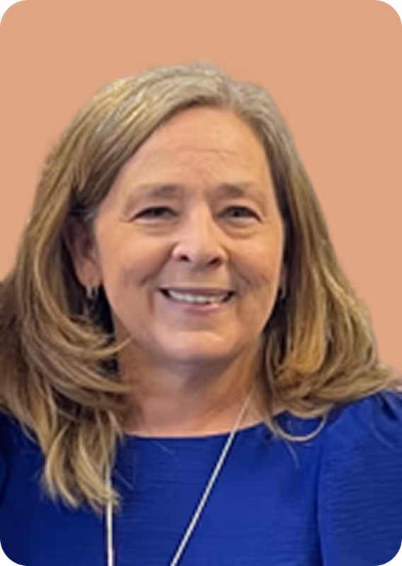 Smiling woman with shoulder-length blonde hair wearing a blue top and necklace on a peach background.