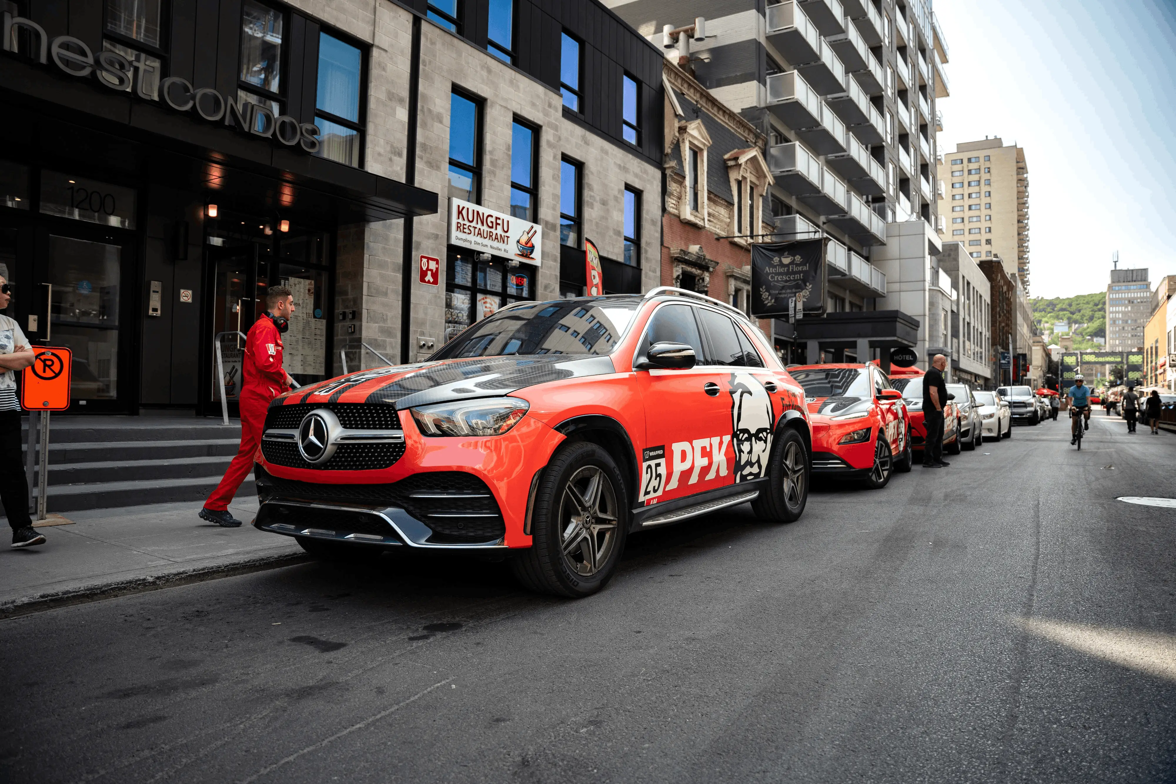 Orange and black Mercedes SUV with PFK branding parked on a city street near a restaurant.