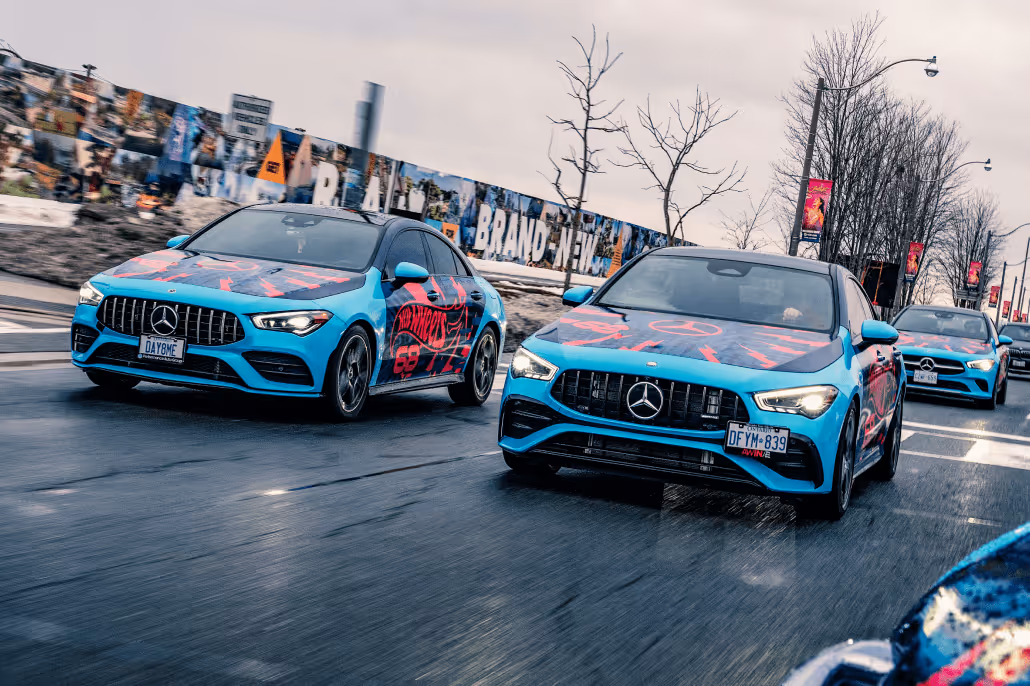 Three blue Mercedes-Benz cars with black and red graphic designs driving on a wet city street.