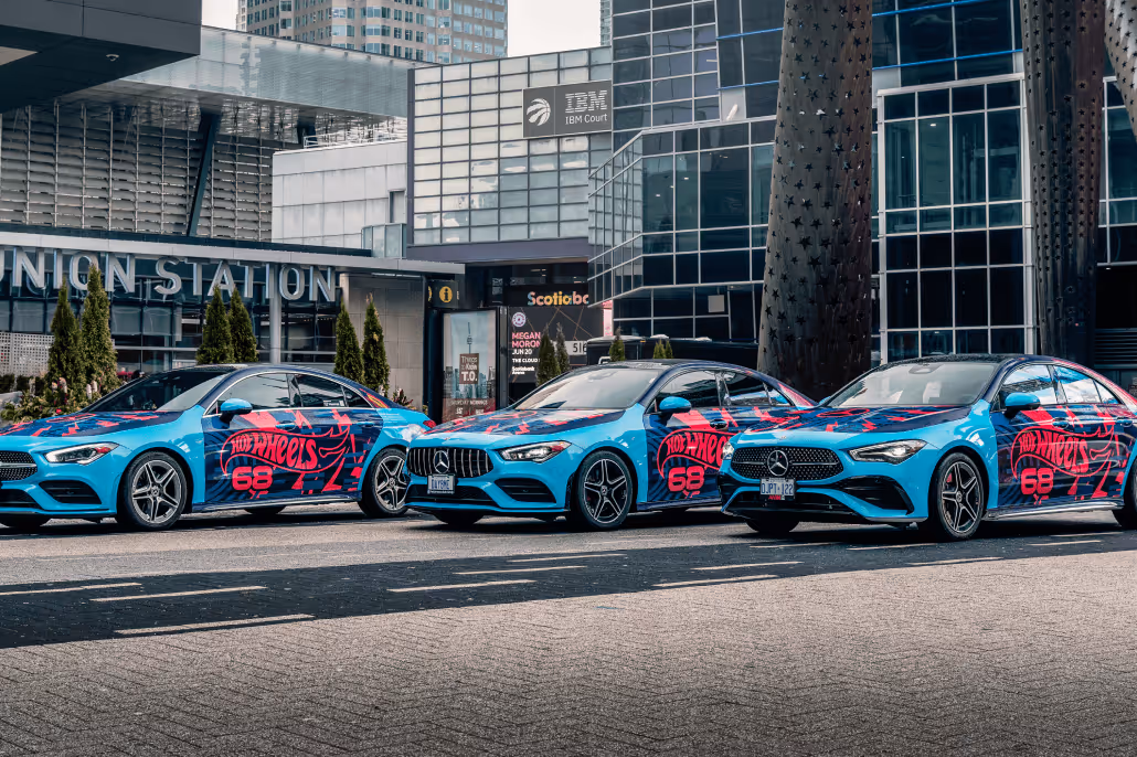 Three blue Mercedes-Benz cars with red Hot Wheels 68 graphics parked in an urban area in front of Union Station and IBM Court buildings.