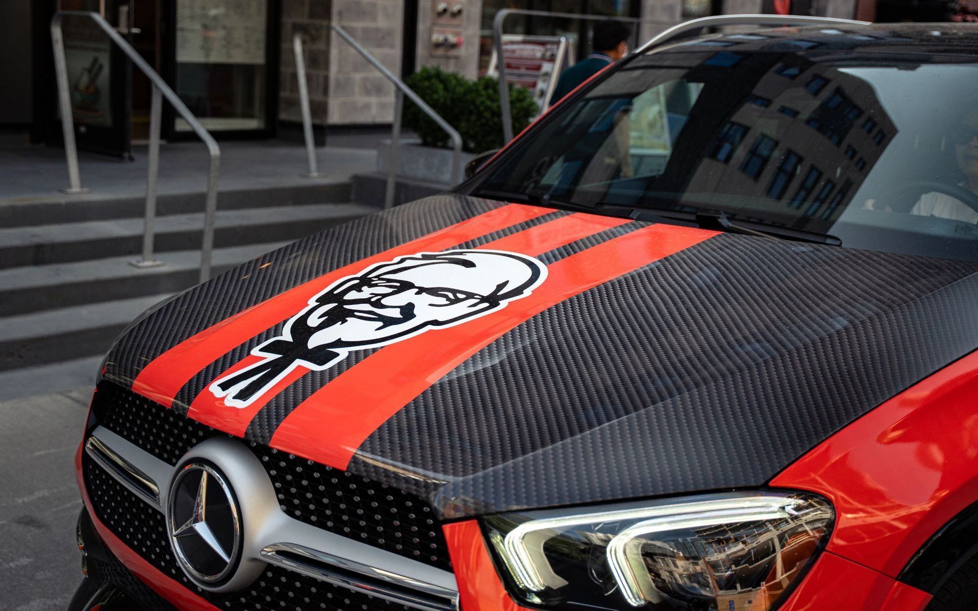 Front view of a Mercedes car with a carbon fiber hood featuring red stripes and a large Colonel Sanders logo.