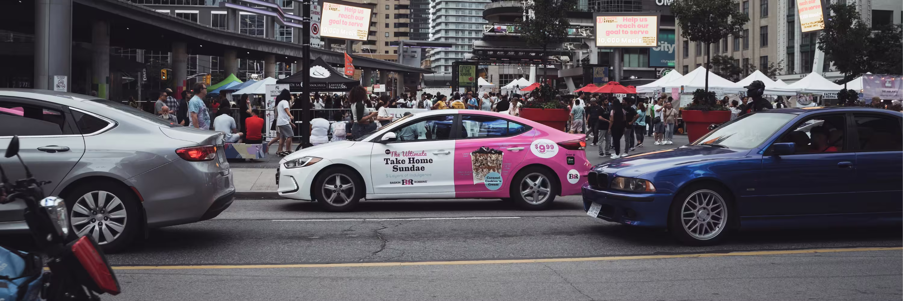 A Baskin Robbins wrapped card driving through a busy street.
