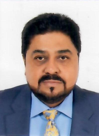 Portrait of a man with dark hair and beard, wearing a blue shirt, patterned yellow tie, and dark suit jacket against a plain white background.