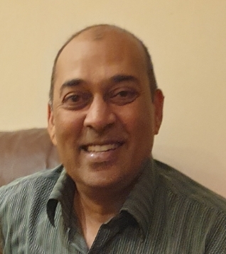 Smiling man with a bald head wearing a green striped shirt seated indoors.