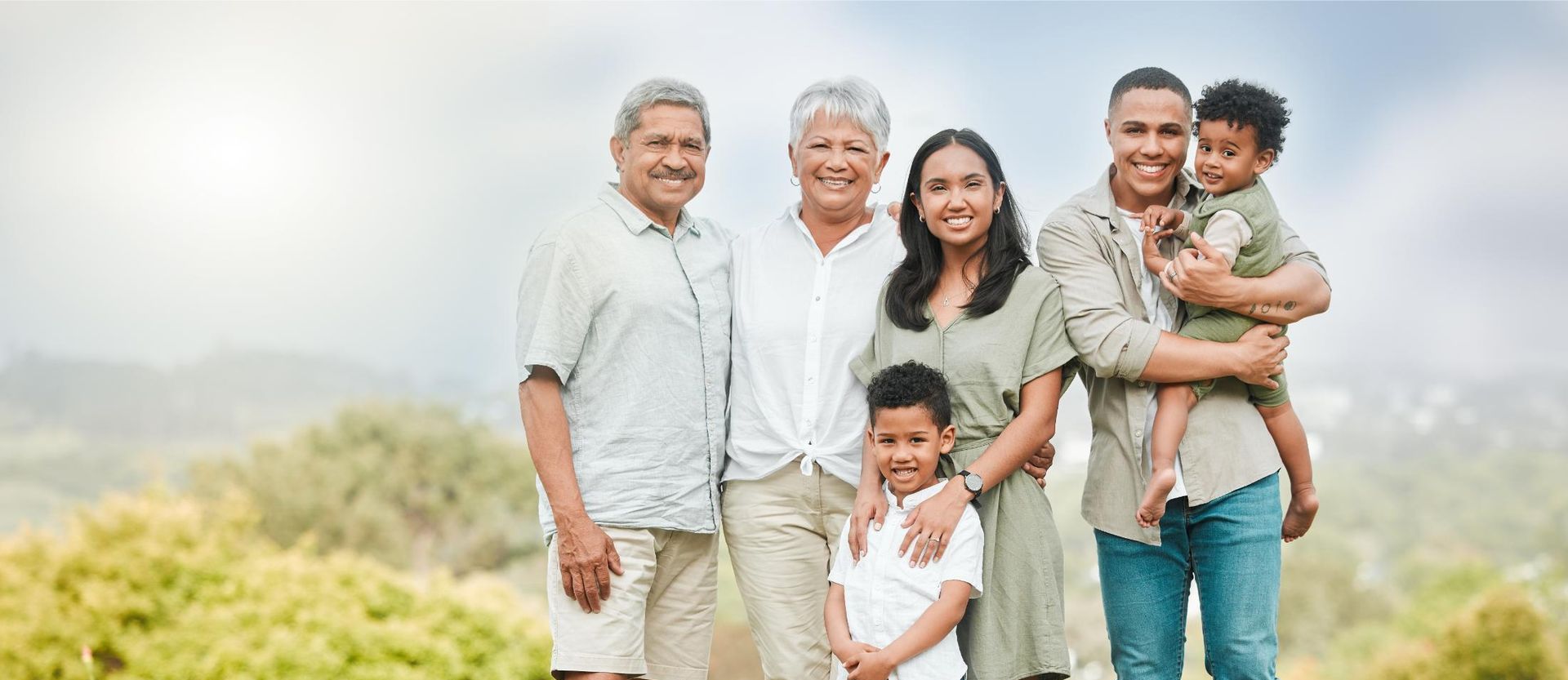 A family of six stands together outdoors, smiling at the camera.