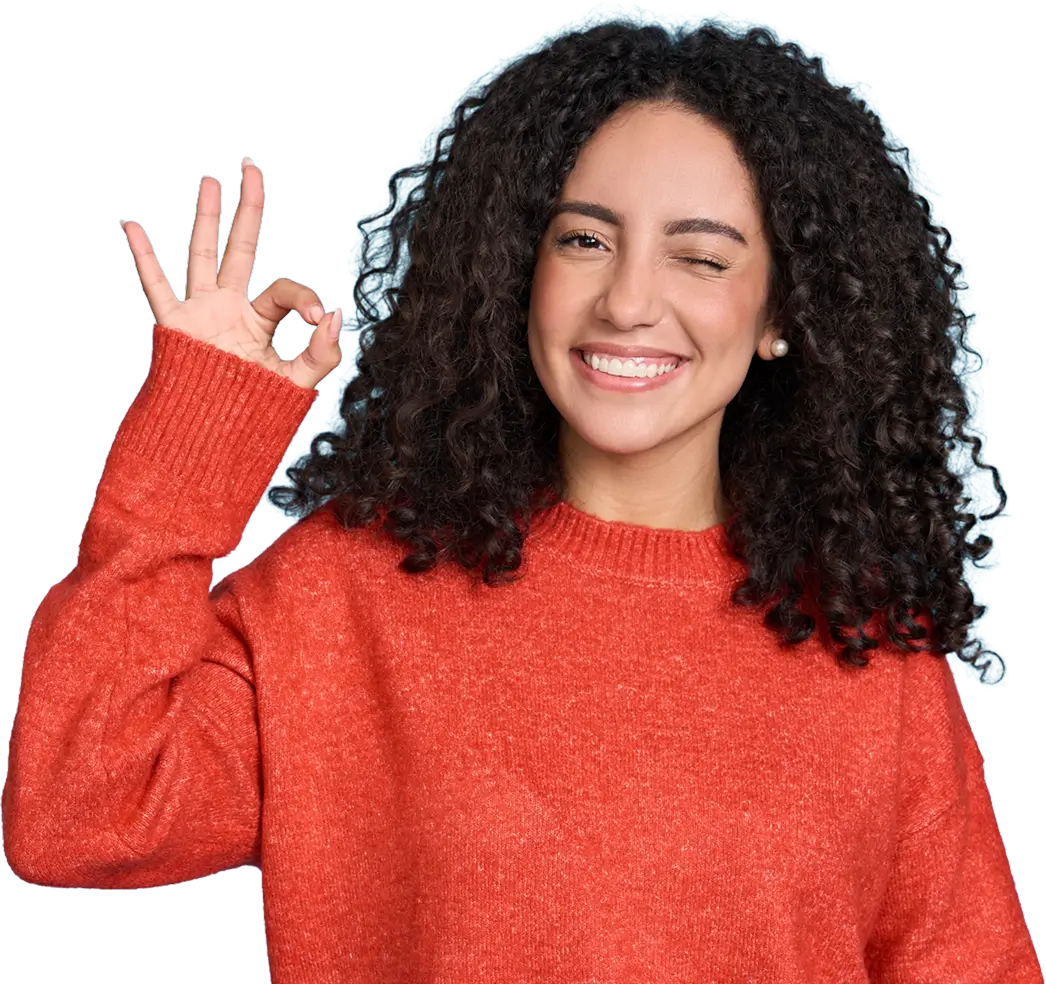 Smiling woman with curly hair wearing a red sweater making an OK hand gesture and winking.