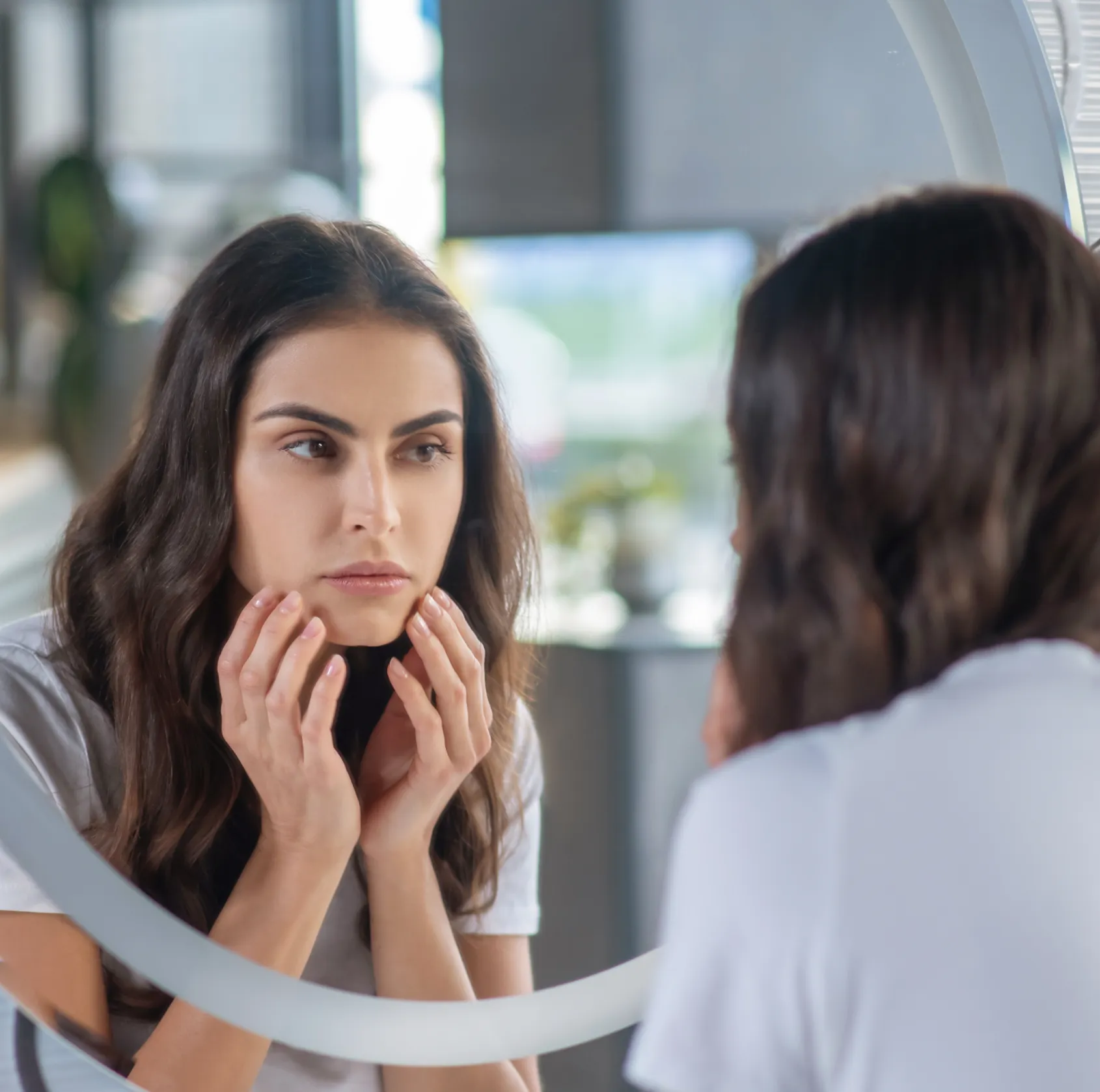 Woman looking at her reflection in a mirror, touching her chin with a concerned expression.