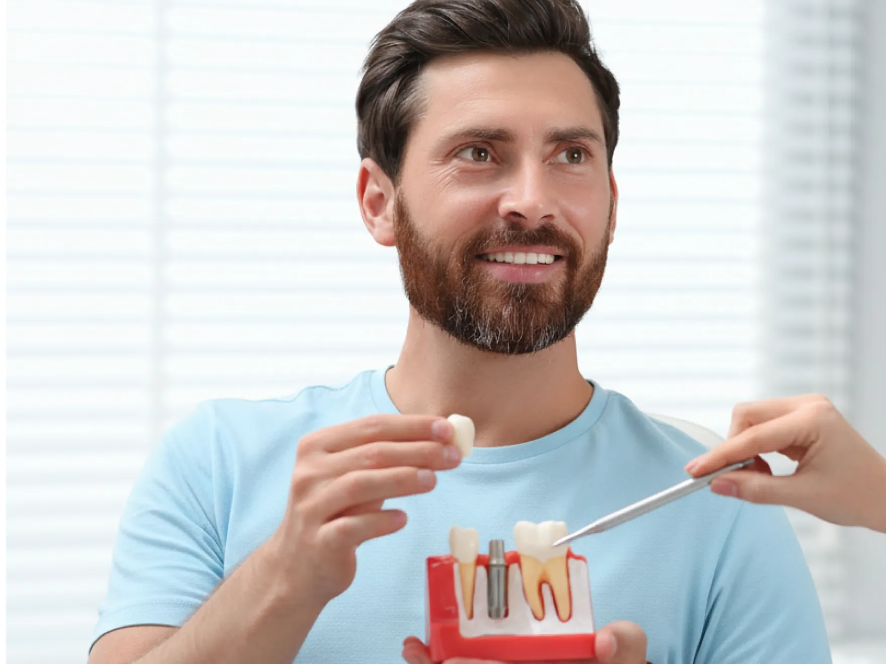 Man holding a dental implant model while a hand points at it with a dental tool.