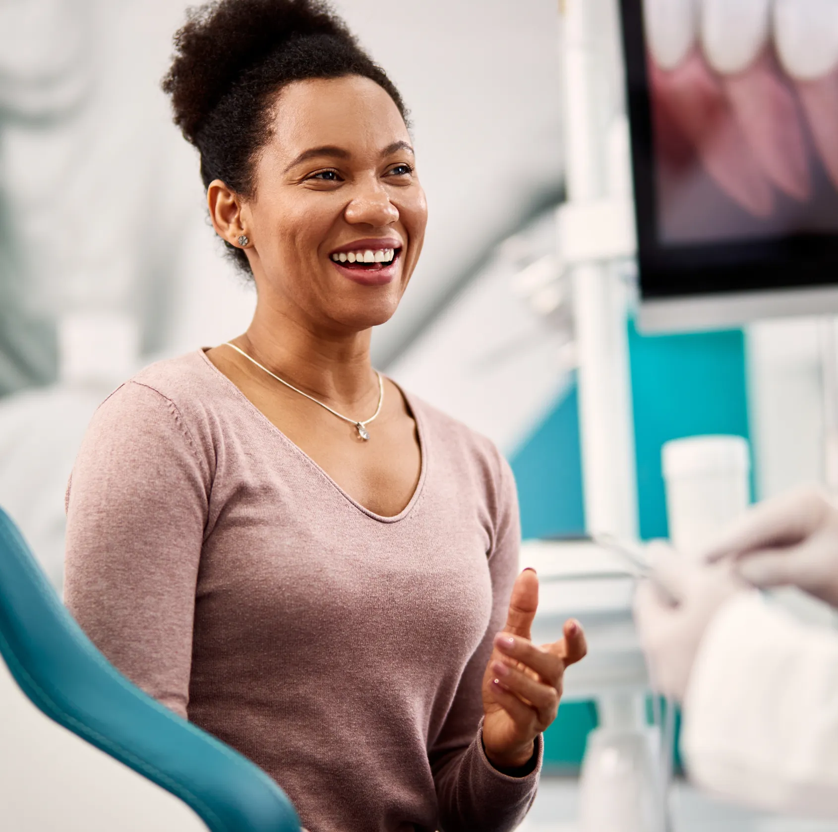 Smiling woman sitting in a dental chair during a dental checkup with a dentist holding dental tools.