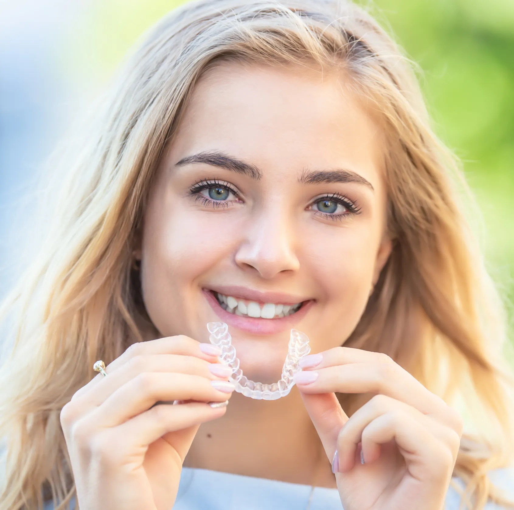 Smiling young woman holding a clear dental aligner in front of her mouth.