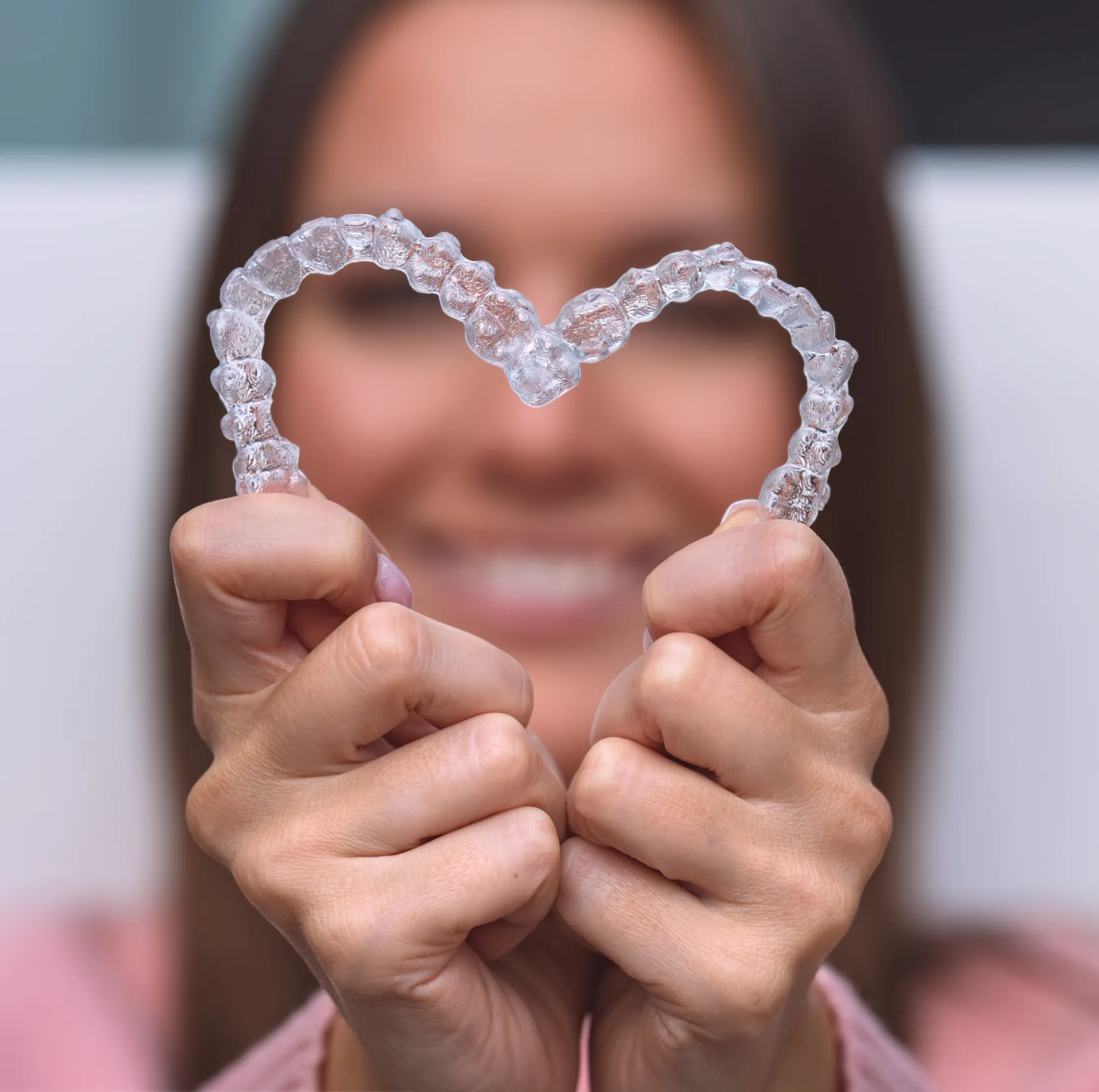 Person holding a transparent dental aligner shaped like a heart in front of their smiling face.