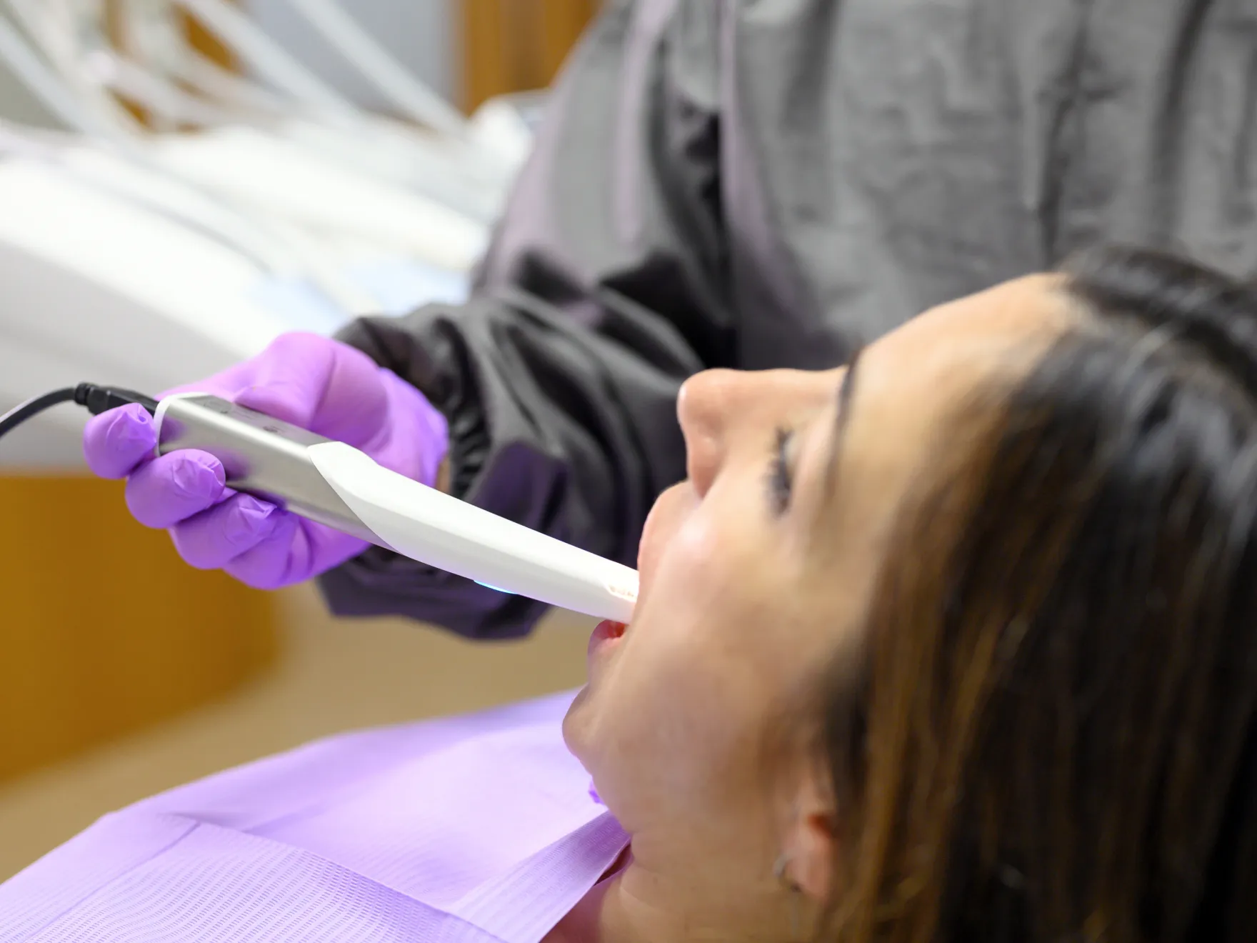 Dental professional wearing purple gloves uses an intraoral scanner inside a patient's mouth during a dental examination.