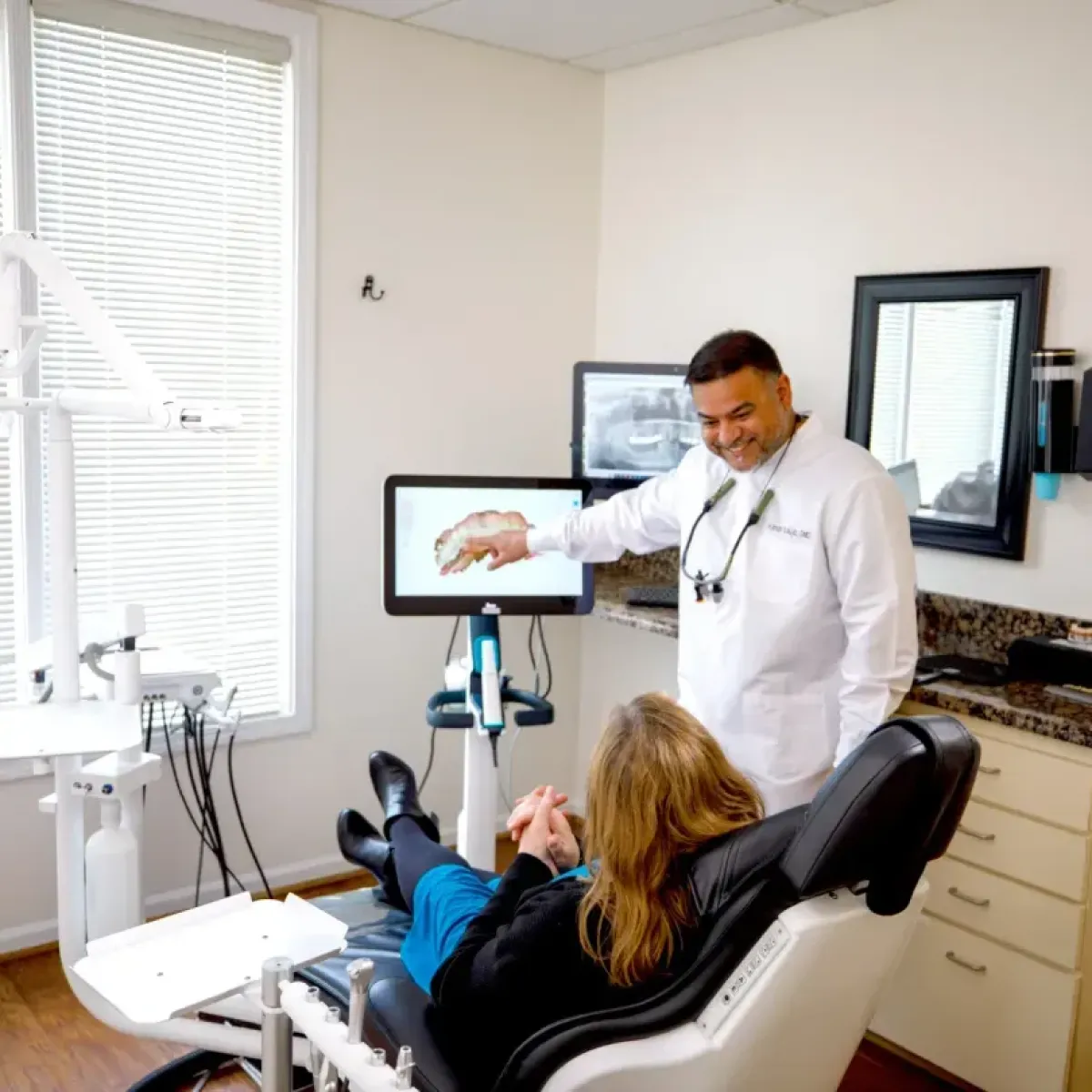 Dentist explaining a dental scan on a monitor to a patient reclining in a dental chair.