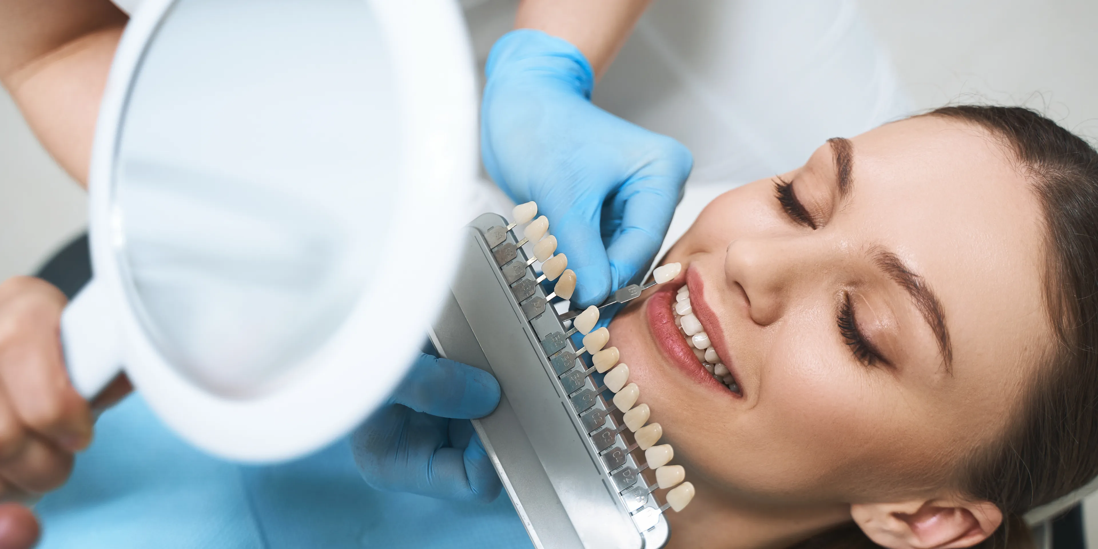 Dentist holding a tooth shade guide next to a smiling woman’s teeth for color matching.