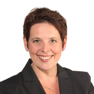 Porträt einer lächelnden Frau mit kurzen braunen Haaren, die einen schwarzen Blazer trägt.