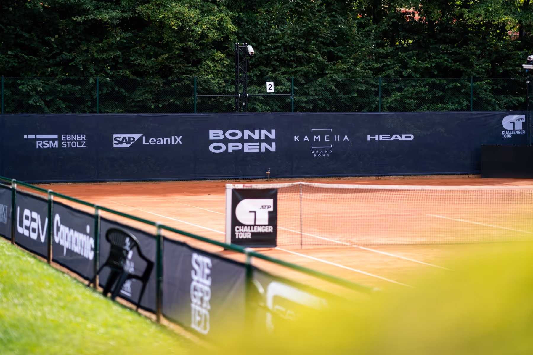 Leerer Tennisplatz mit roten Sand, gesäumt von schwarzen Bannern mit Sponsorenlogos für Bonn Open und ATP Challenger Tour.