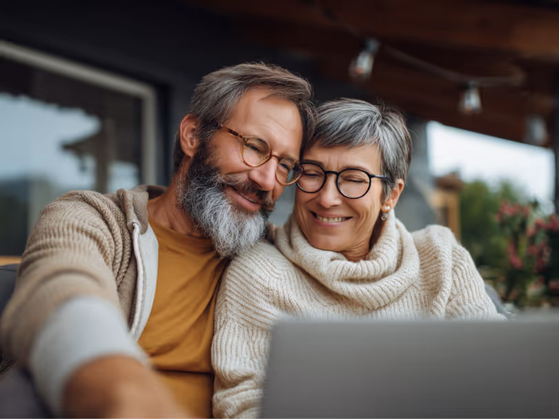 Smiling older couple wearing glasses looking at a laptop together indoors.