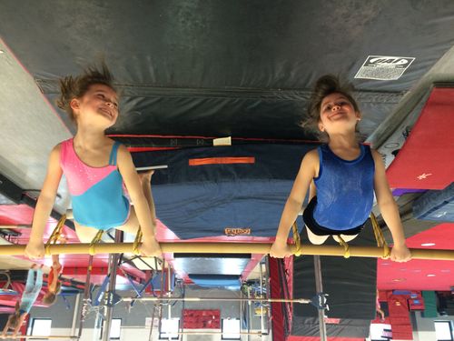 Two young gymnasts smiling as they swing on the bars at Dynamite Gymnastics Center in North Bethesda, MD