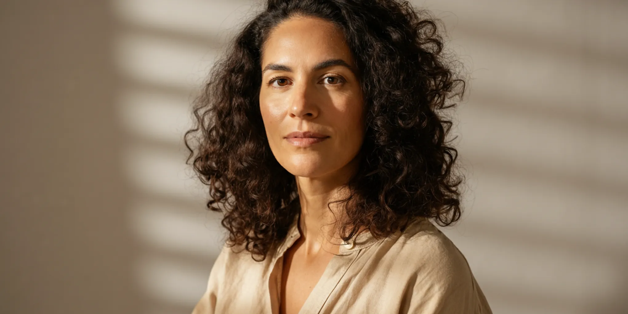 Portrait of a woman with curly hair looking thoughtfully at the camera.