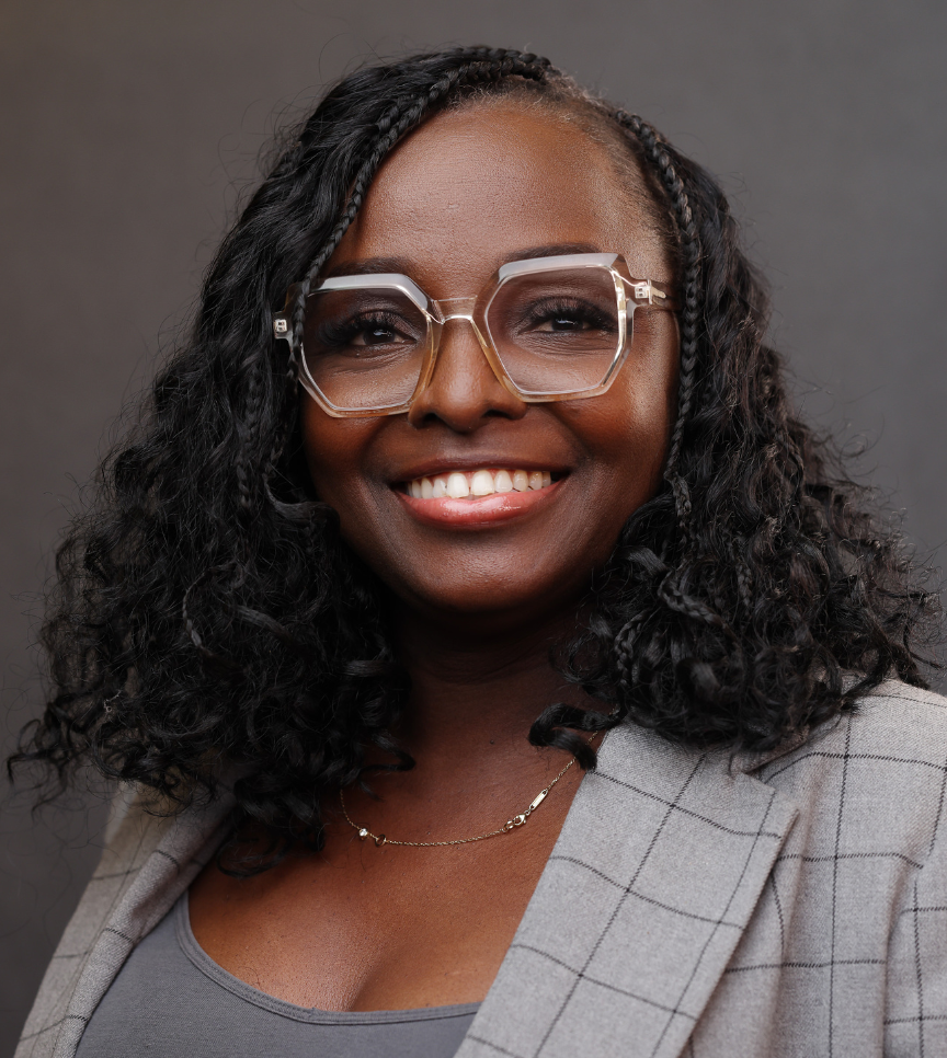 Smiling woman with curly hair, large glasses, a gray checkered jacket.