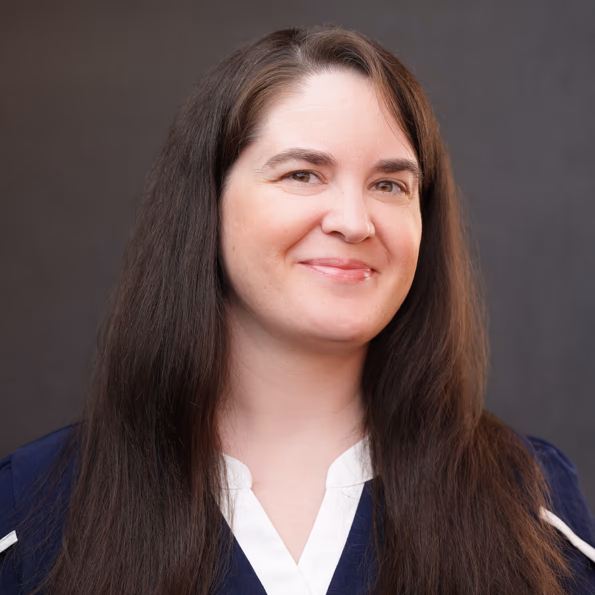 Smiling woman with long dark hair wearing a navy blue top.