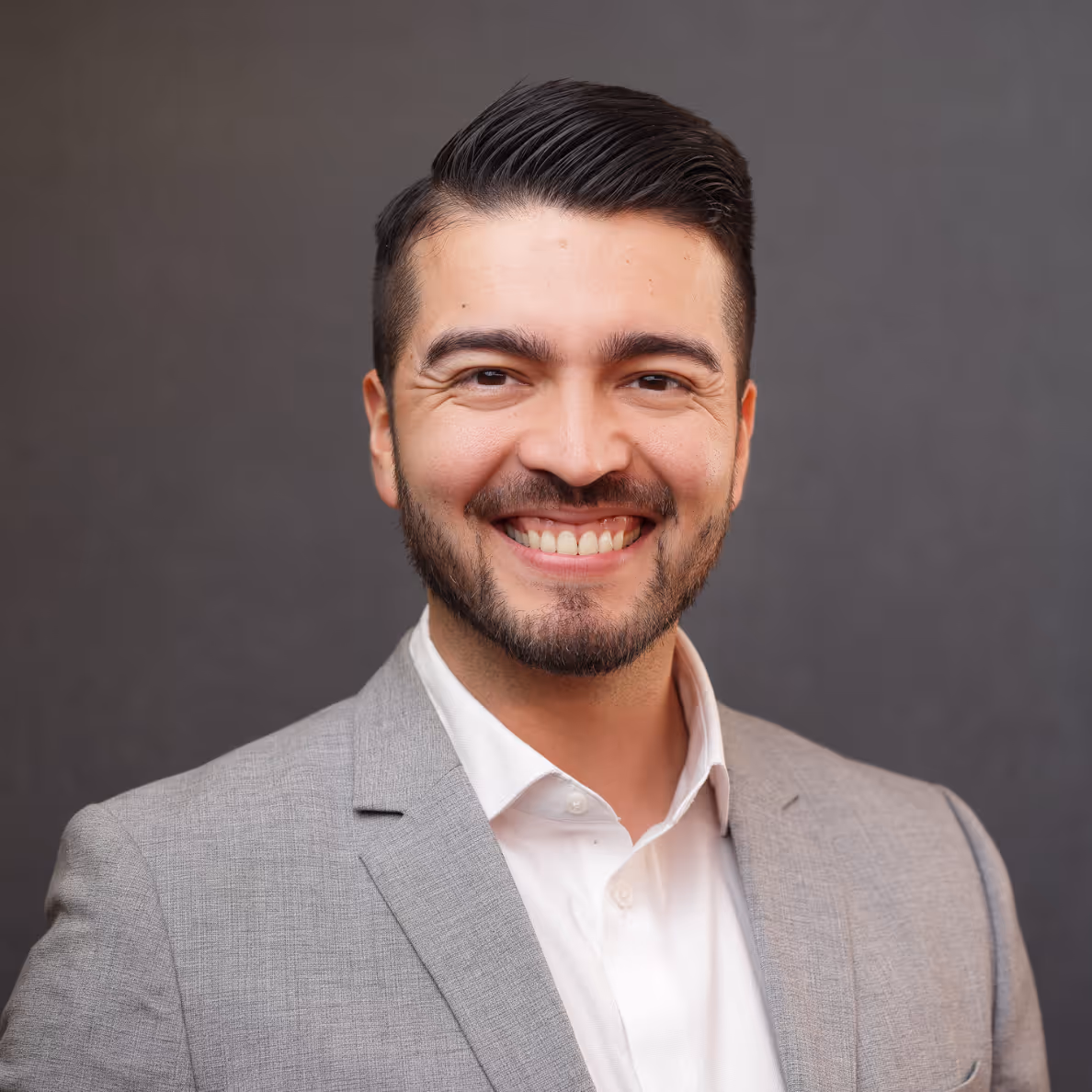 Man with trimmed beard wearing a light gray suit jacket and white shirt