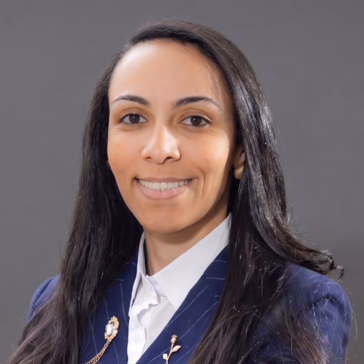 Smiling woman with long dark hair wearing a blue blazer and white shirt.