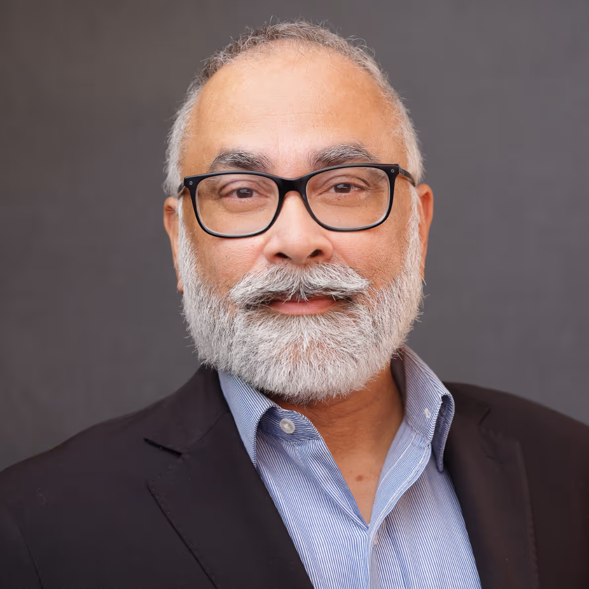 Smiling middle-aged man with white beard and glasses wearing a suit jacket and blue shirt.