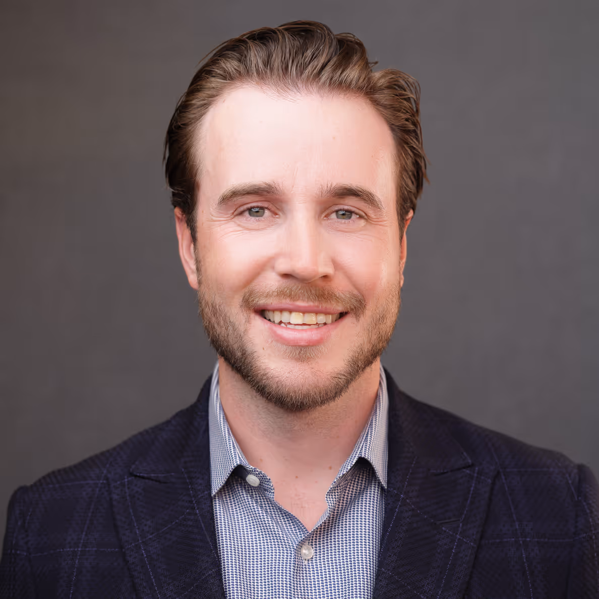 Smiling man with light beard, wearing a blue checkered shirt.