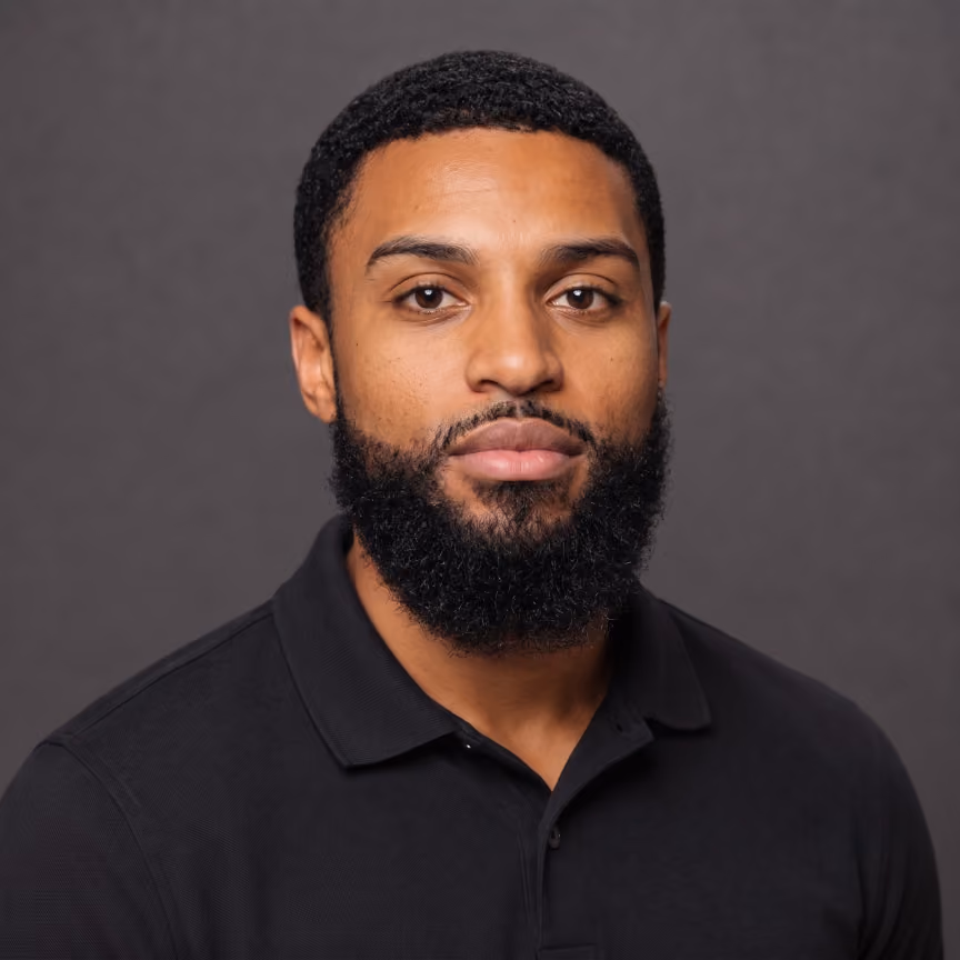 Portrait of a man with short curly hair and a full beard wearing a black collared shirt.