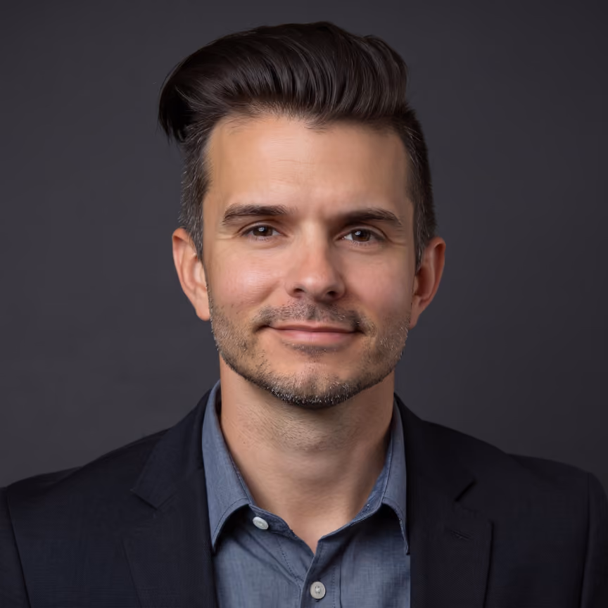 Portrait of a man with styled dark hair wearing a dark blazer and blue button-up shirt.