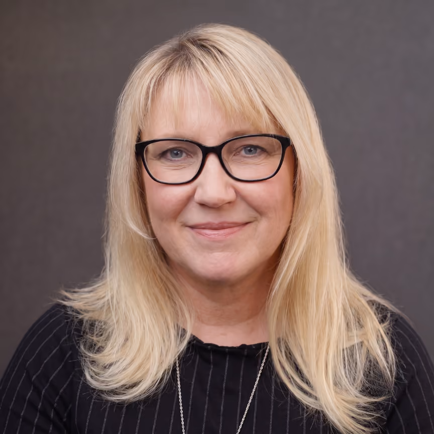 Smiling woman with long blonde hair wearing black glasses and a black pinstriped top.