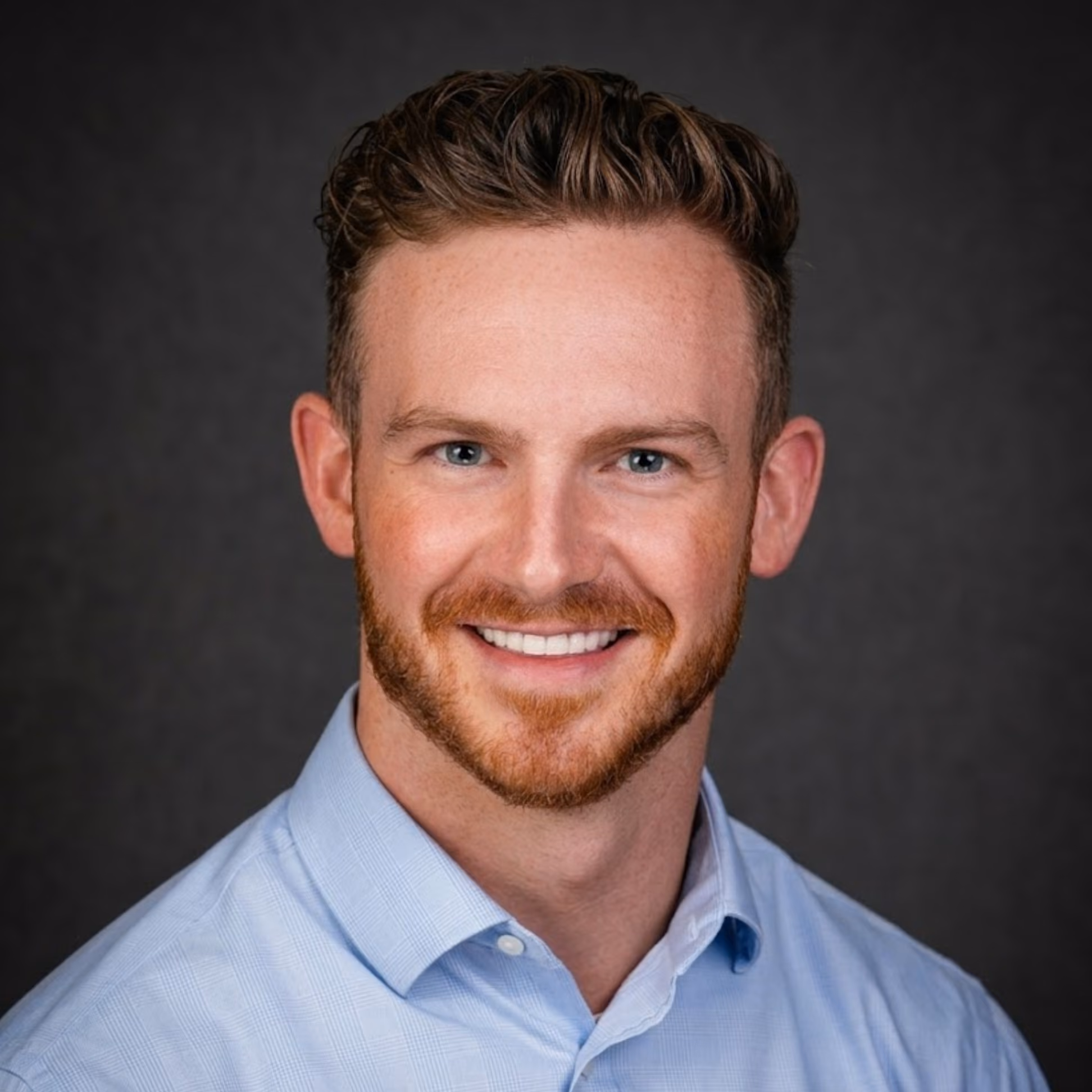 Smiling man with blue eyes, red hair, beard, wearing a light blue shirt.