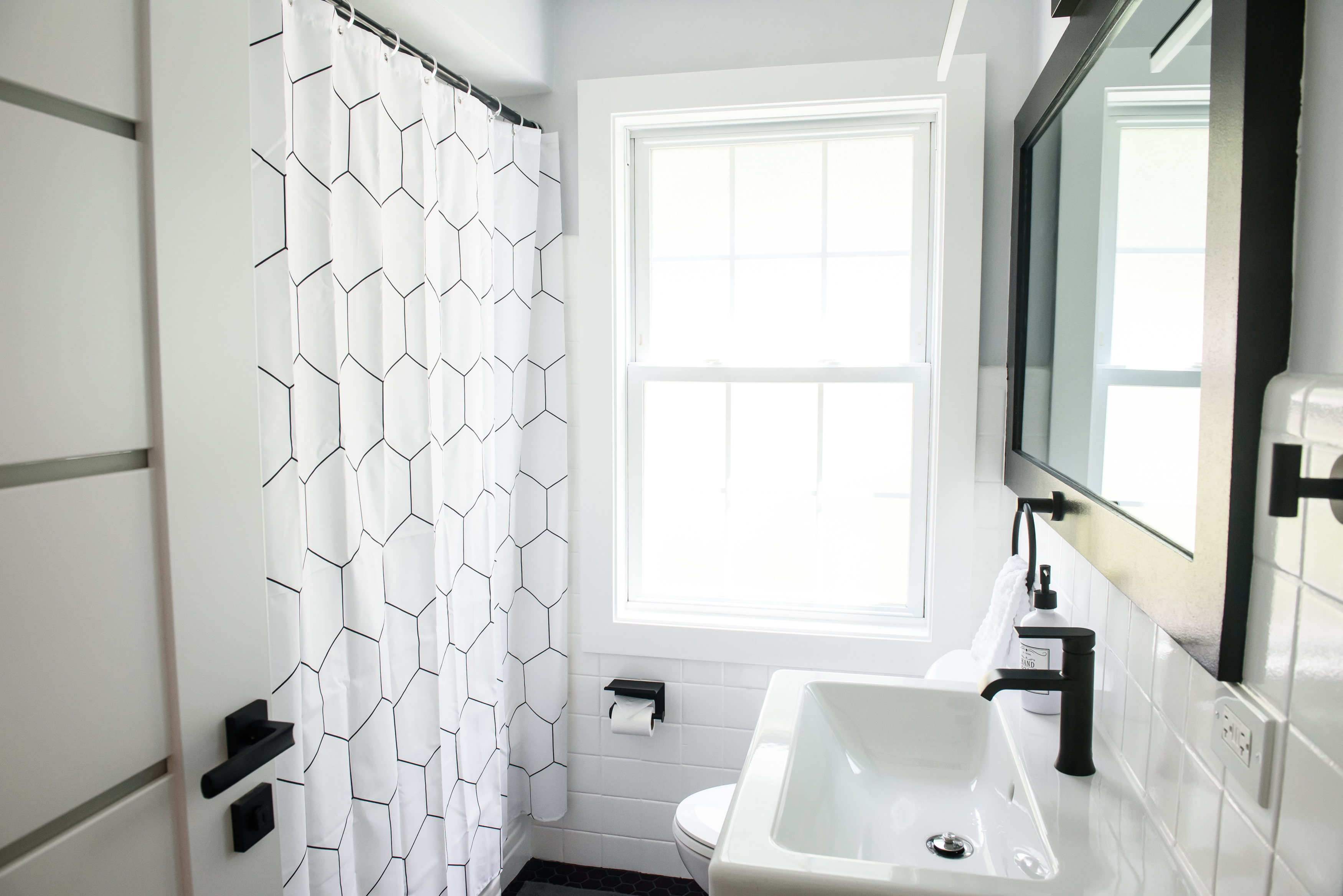 Bright modern bathroom with a white geometric shower curtain, rectangular sink with black faucet, and a window letting in natural light.