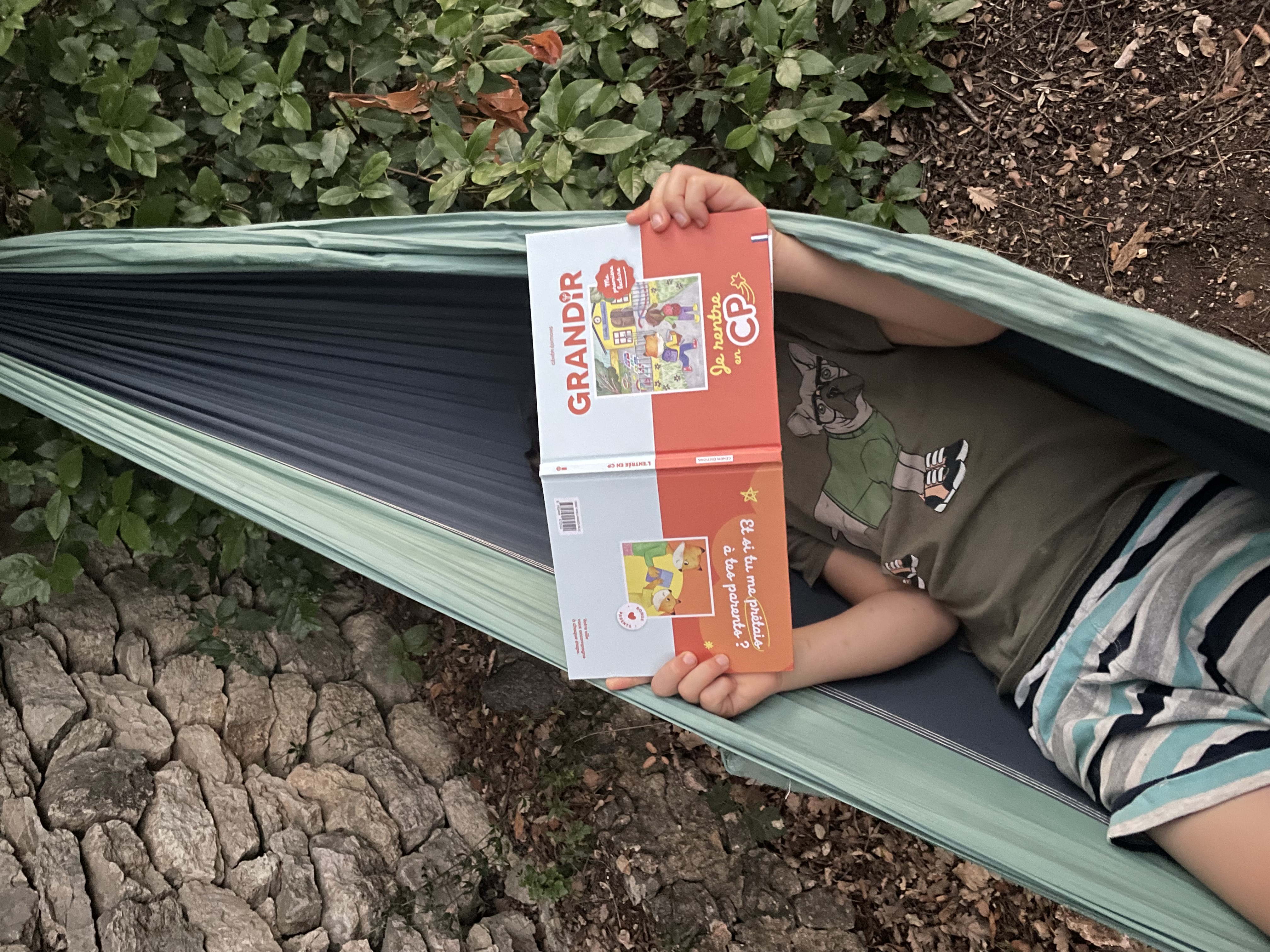 Un enfant lit GRANDIR, le guide de l’entrée au CP, allongé dans un hamac