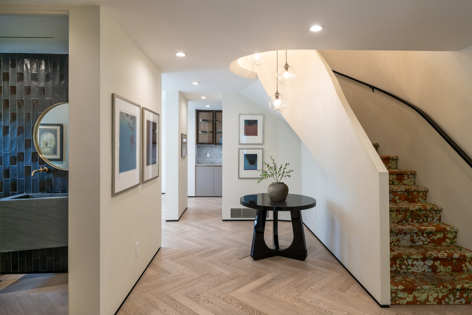 Residential hallway interior with curved staircase and herringbone flooring.