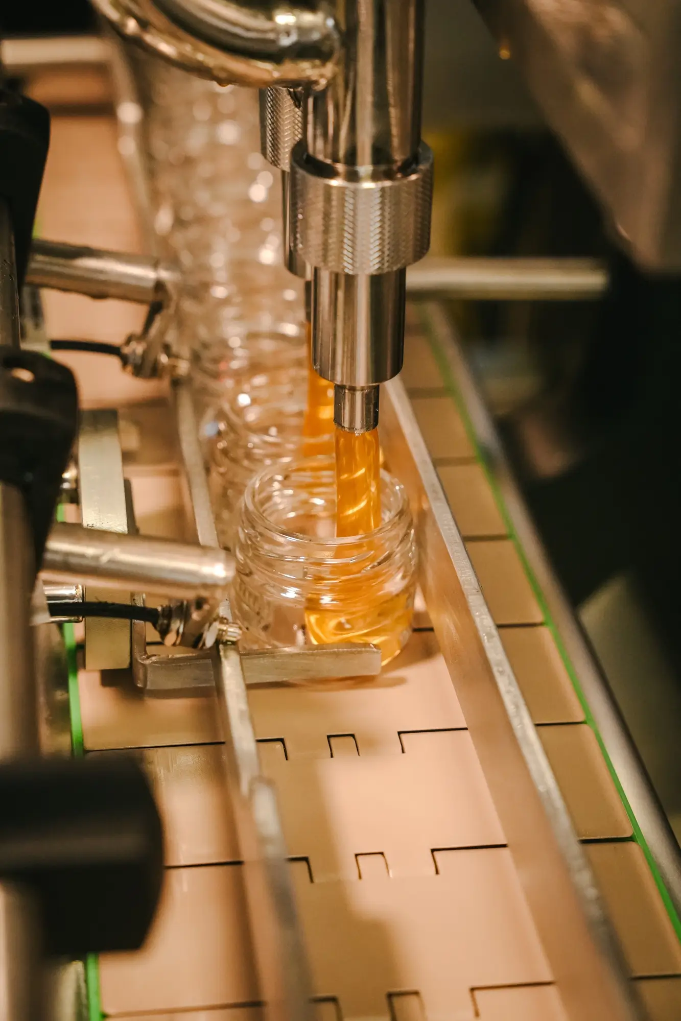 Honey being dispensed into a small glass jar on an automated filling machine.