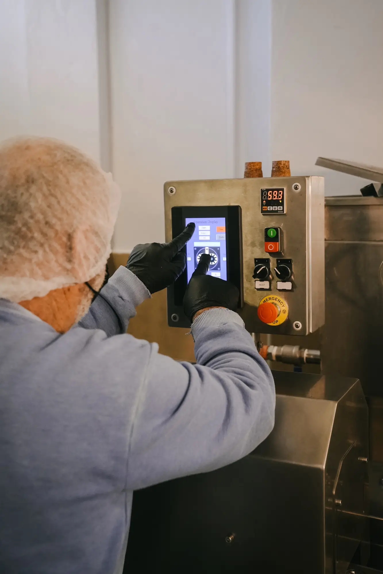 Person wearing hairnet and gloves operating a touchscreen control panel on industrial machinery.
