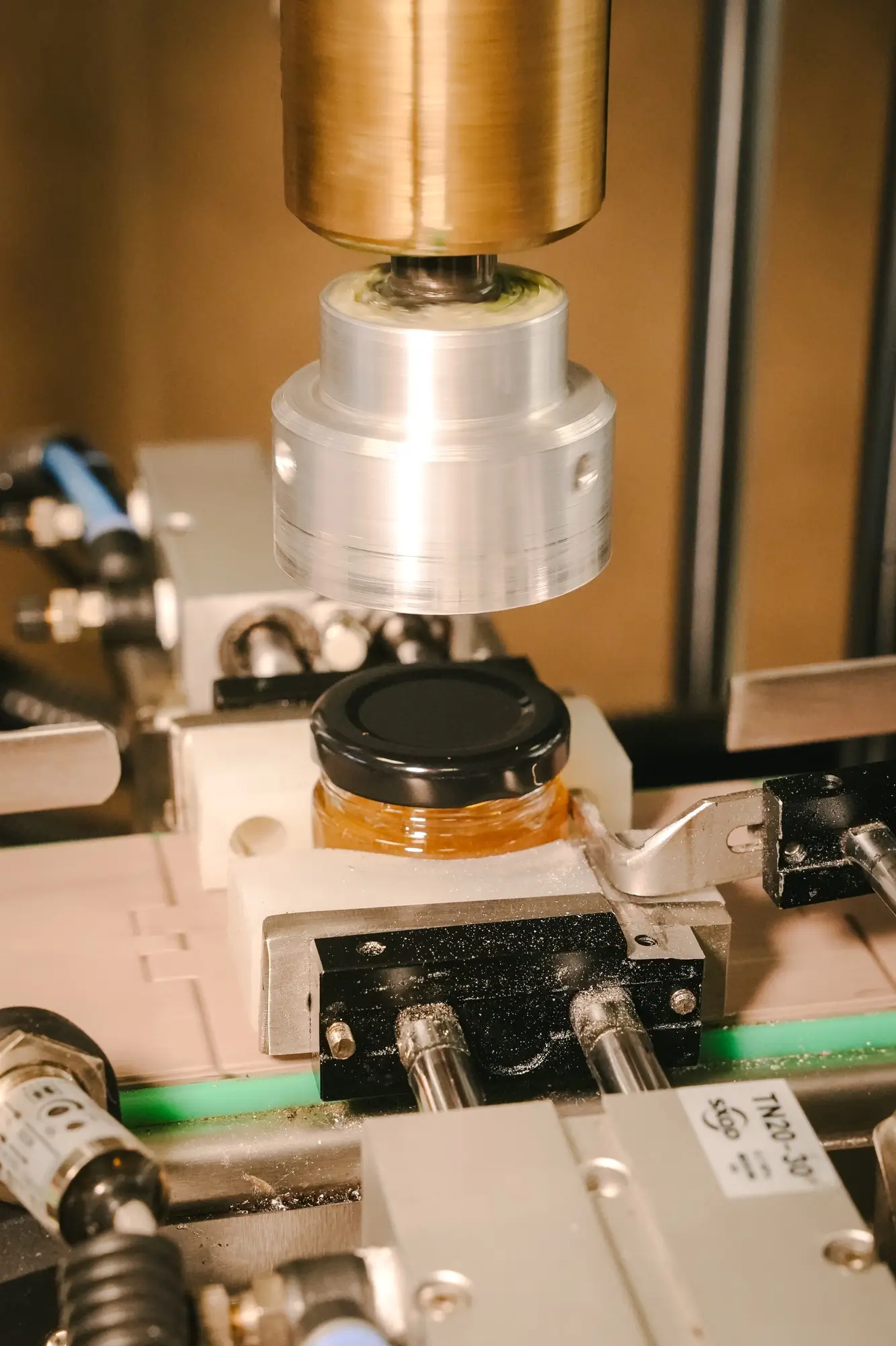 Automatic machine sealing a black lid on a small jar of honey.