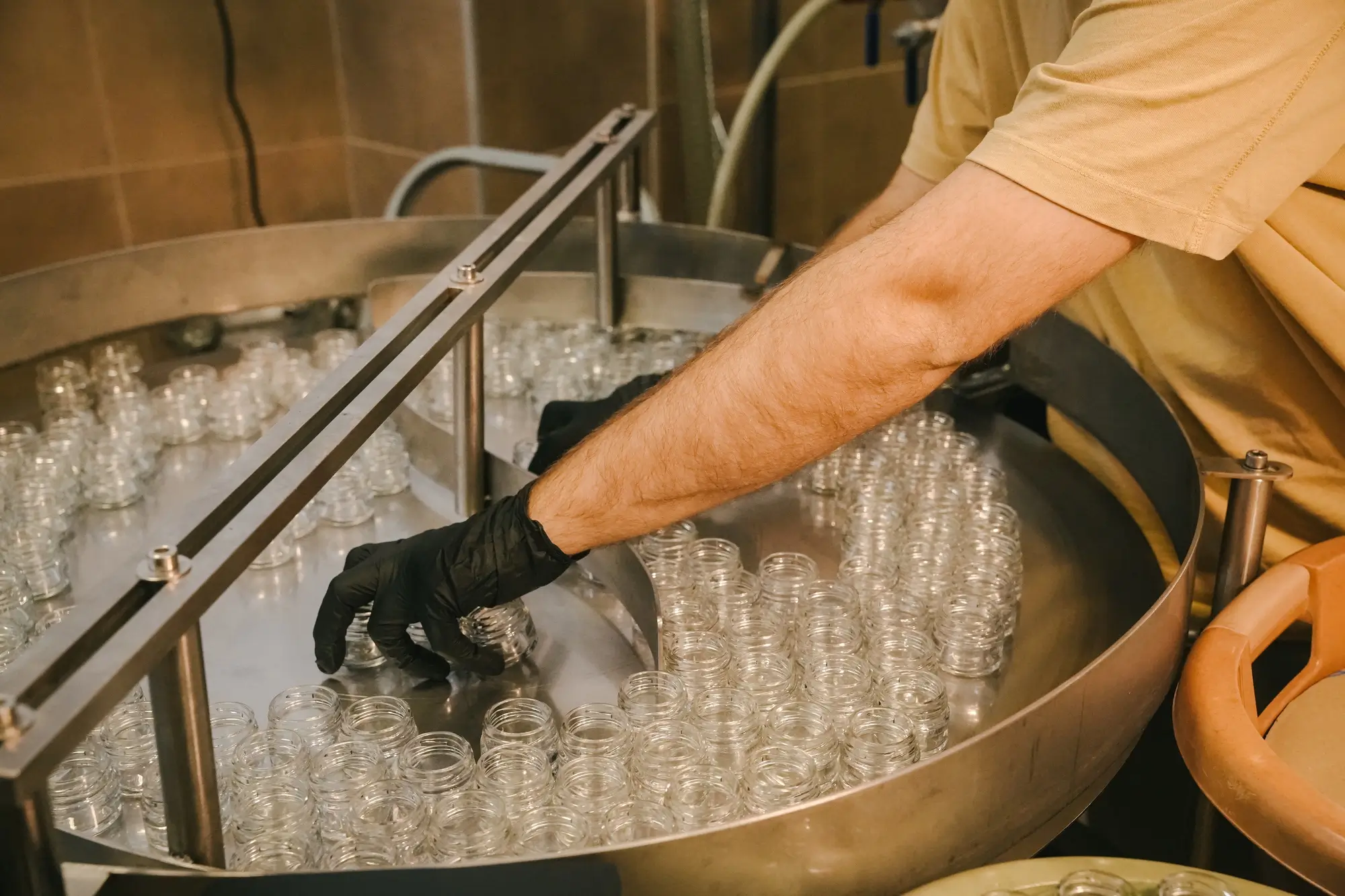Person with black glove organizing empty glass jars on a metal production line.